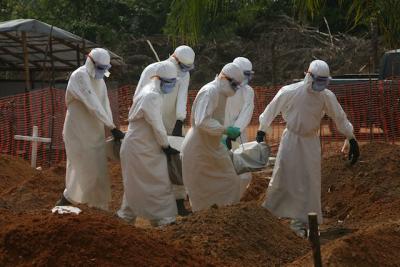 Members of the decontamination team carry the body of Delecia Pentee Jaffan, 33, and past fresh graves at Disco Hill, an hour's drive outside Monrovia, Liberia, on Jan. 8, 2015. Disco Hill is a new 25-acre graveyard just purchased by the Liberian government and operated by the US-based nonprofit Global Communities. Jaffan's body will be buried in the Christian section of the cemetery. The site also has separate, reserved space for Muslim burials. BY CHERYL HATCH/COPYRIGHT 2015