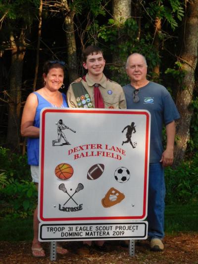 Dominic Mattera (center) poses with his parents, Debbie and Al, behind the sign he designed. Photo by: Grace Ballenger