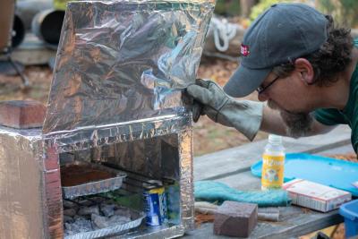 Scout Leader Ed Brown checks on his brownies cooking inside a foil-covered cardboard oven. Photo by: Sawyer Smook-Pollitt