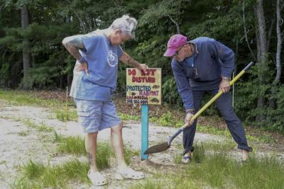 Intern and Volunteer Coordinator, Billie-Joe Gibbons, left, holds a turtle sign as Jay Whitestone, a volunteer, pounds the sign into the sand near turtle nests.