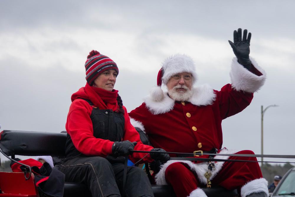 Santa Claus waves from atop a horse-drawn carriage.