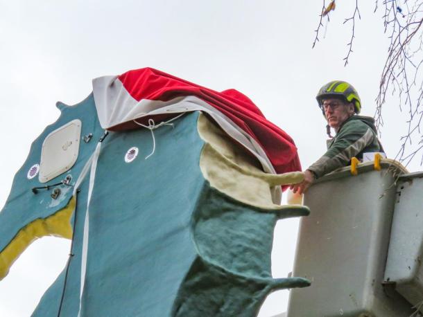 G. B. Knowles used his landscaping equipment to reach the top of the statue and install the new hat Dec. 6.  Photos by Grace Roche