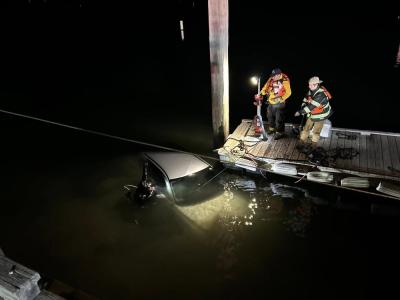 The crew looks at the car in the water.