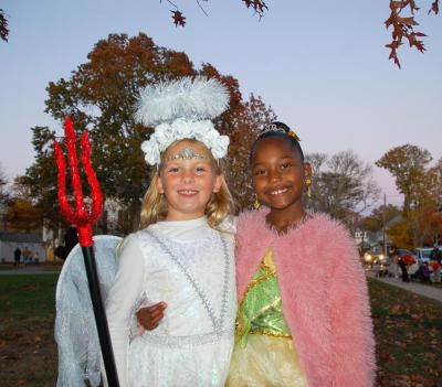 Ivy Stewart, 8, as a half angel-half devil and Nina Lyman, 8, as Princess Tiana at the Mattapoisett Halloween parade smile together. Photo by Mari Huglin 