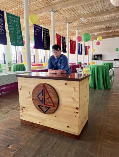 Josh Van Inwegen stands behind the welcome desk he built for the Community Boating Center of New Bedford.