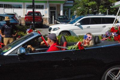 Courtney Nowick, right, smiles from a convertible decorated with flowers and flags.