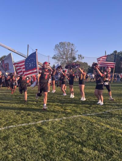 The football team runs through a banner amid rows of cheerleaders as they enter the field before the game.
