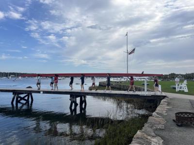 The team of eight boys, plus a coxswain, walks a boat to the waters of Sippican Harbor. Photo by Grace Roche