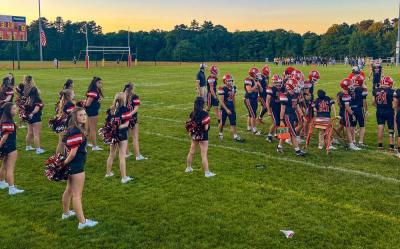 The team stands on the sidelines behind the football players.