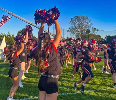 Cheerleaders welcome the football team onto the field before the game.