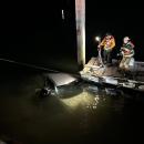 The crew looks at the car in the water.