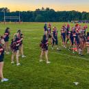 The team stands on the sidelines behind the football players.