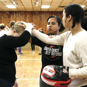 Mattapoisett Officer Linera Lima helps self-defense class attendees Leilani DePina and Joseline Lima learn how to defend themselves in a hair-pulling scenario in February. Photo by Grace Ann Natanawan