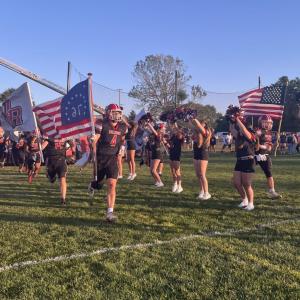 The football team runs through a banner amid rows of cheerleaders as they enter the field before the game.