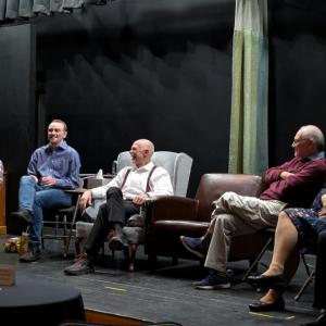 A group of actors sits on the stage during a scene in the play "The Attorney in Fact"