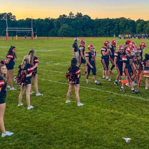 The team stands on the sidelines behind the football players.