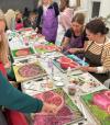 A table of artists paint pomegranates on silk