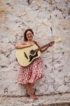 sara achorn stands against a wall with her guitar 